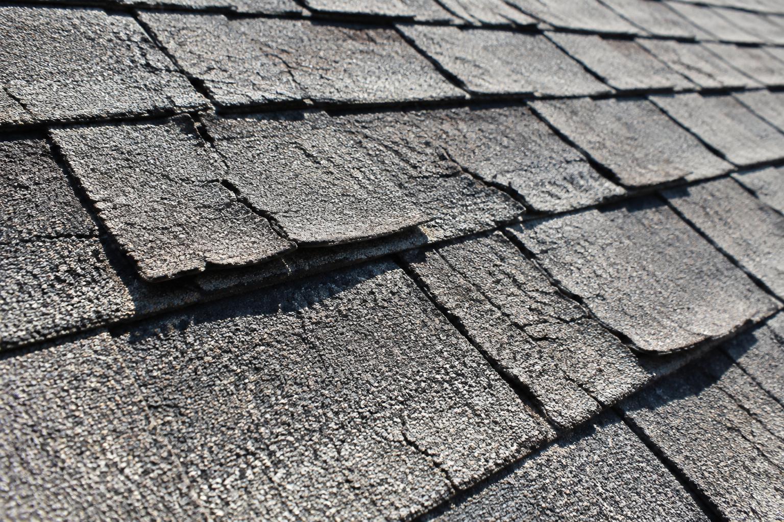 Close-up of dry, gray asphalt shingles with cracking and curling edges